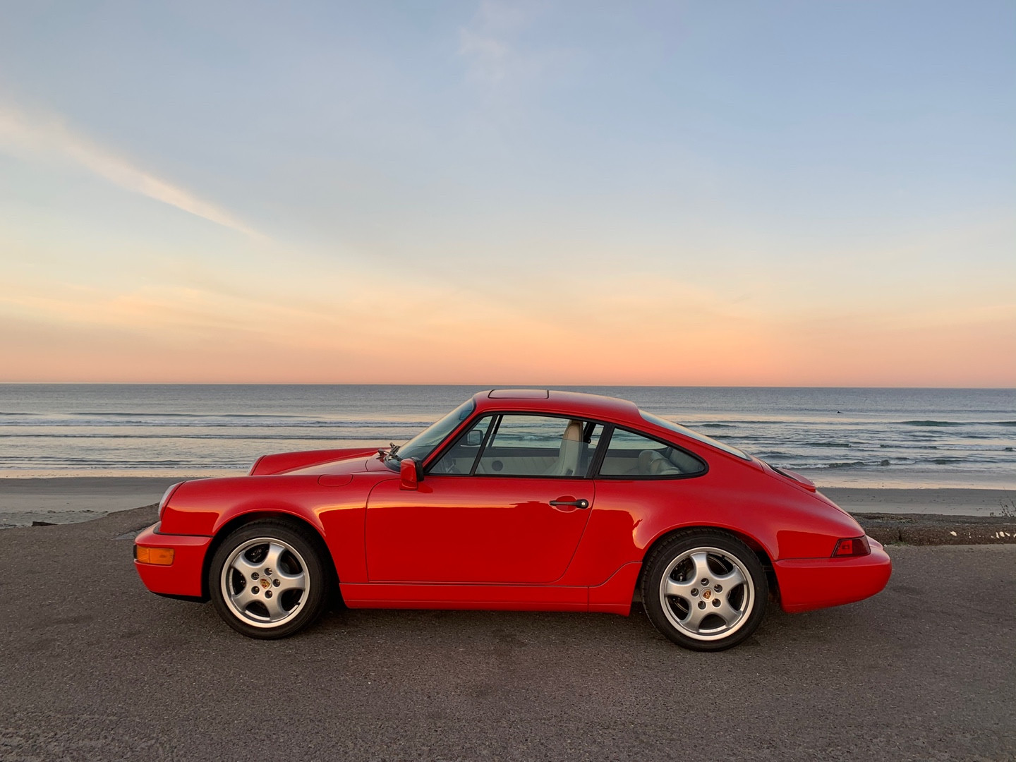 A red 911 against the sea and evening sky.