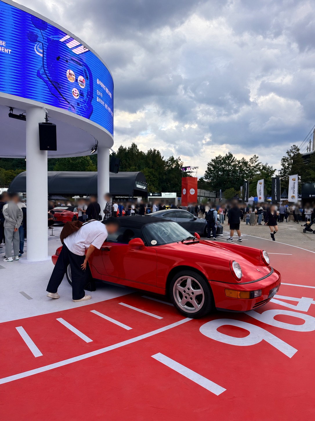 A red air-cooled Porsche Cabriolet. Faces blurred for privacy.